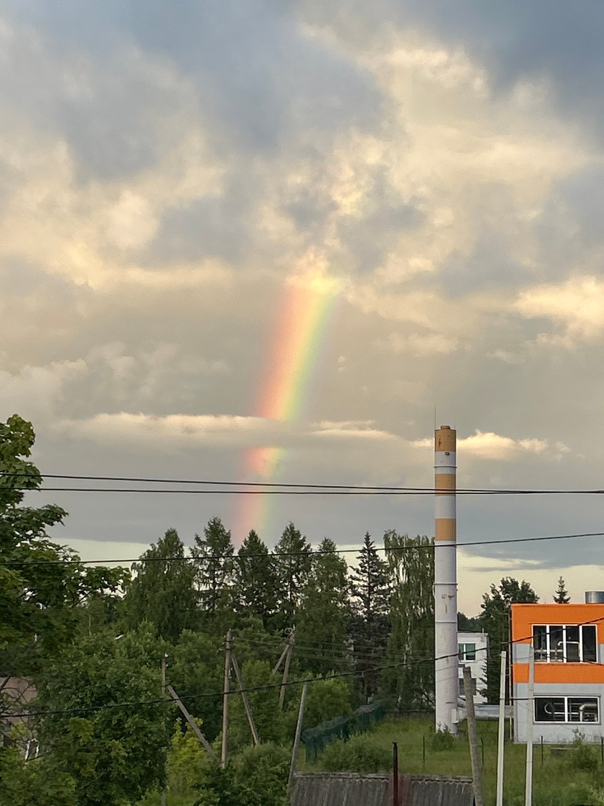 Rainbow over a striped industrial chimney in rural Russia