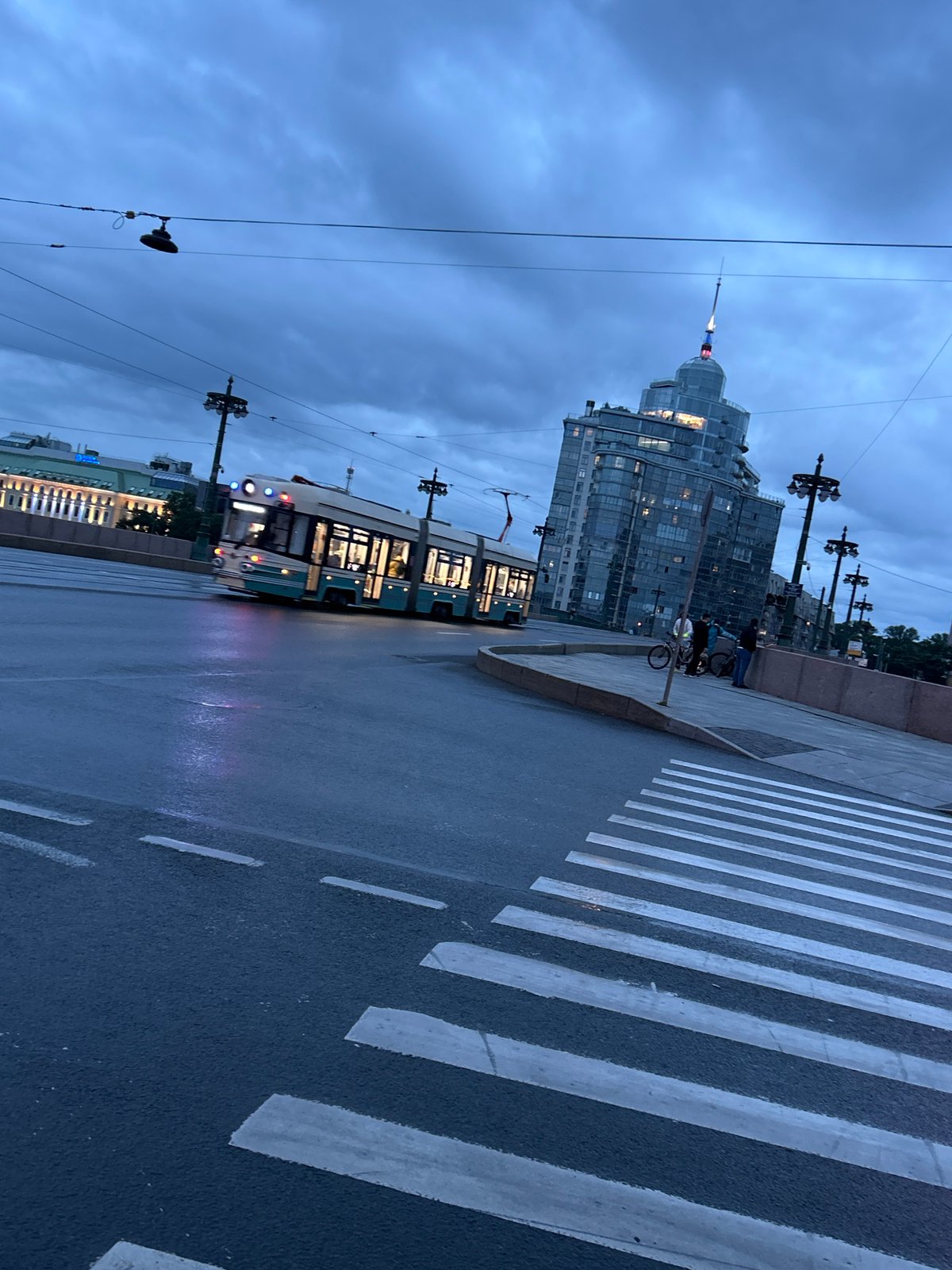 Street cleaning crew works wet pavements outside classical city building at dusk