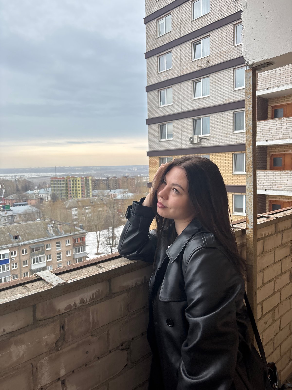 Woman gazes over cityscape from windowsill in Perm