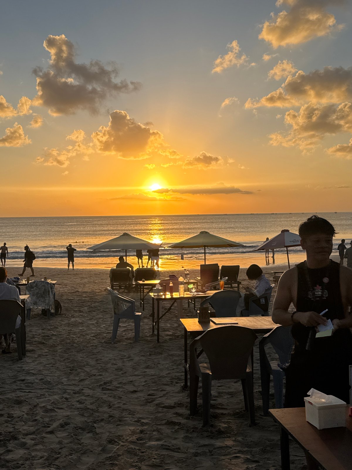 Golden hour on Kuta Beach with planes, waves, and beachgoers