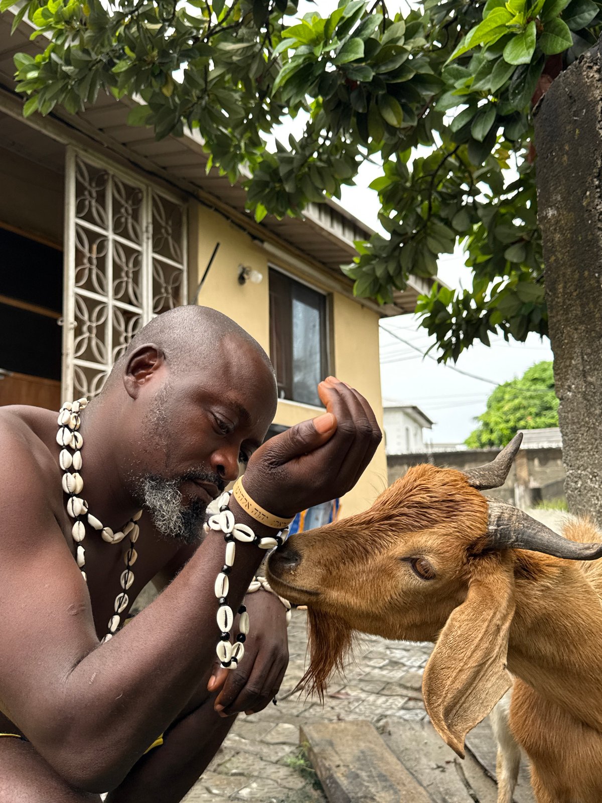 Man with traditional jewelry tends goat in Ado, Nigeria
