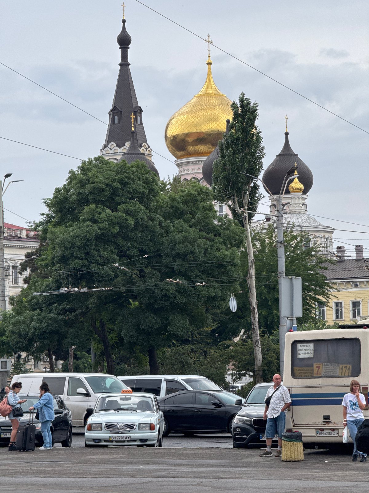 Group gathered near vehicles, church domes visible in urban background