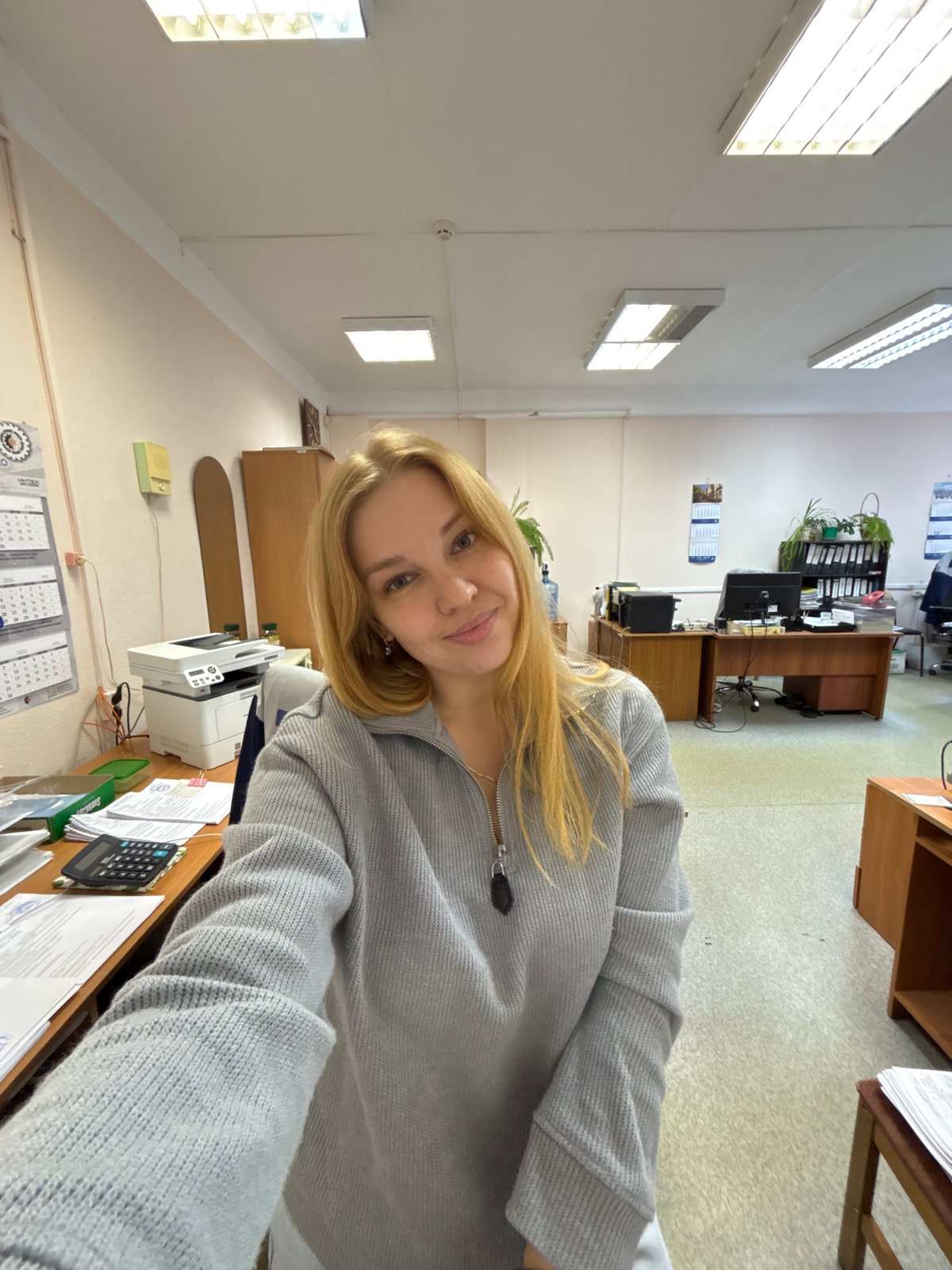 Woman takes office selfies wearing gray sweater, purple wristband