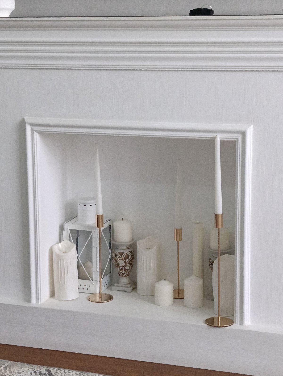 White mantelpiece styled with candles, lantern, and vase