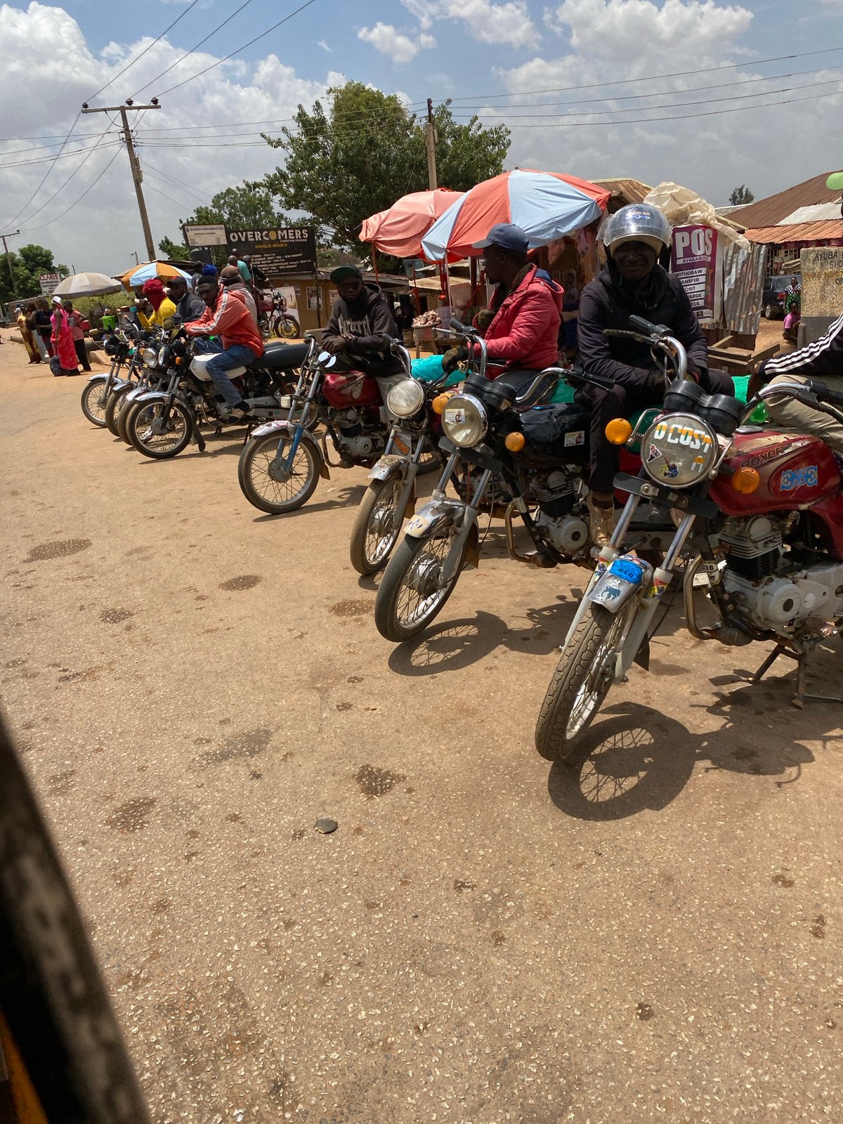 Motorcycles with riders gather on Bukuru street
