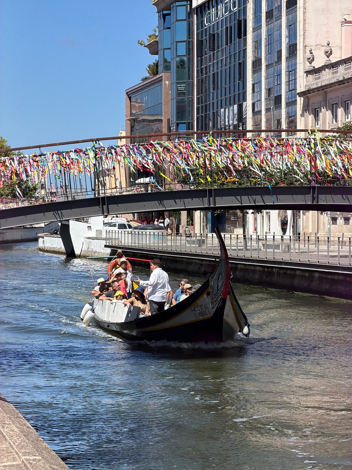 Tourist boat tours Aveiro's ribbon-decorated canal bridges on sunny morning