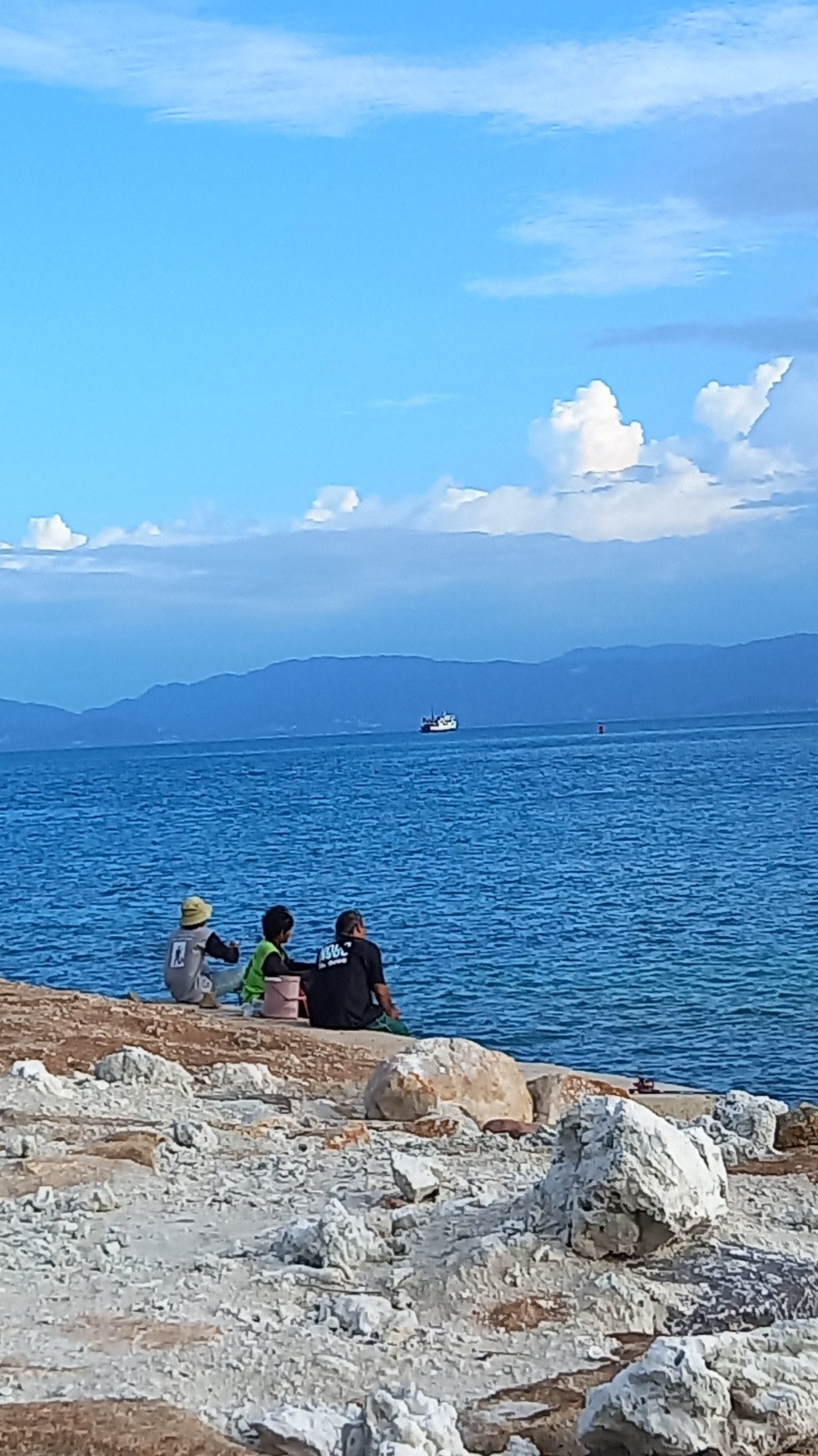 Three people rest on rocky shore in Koh Phangan