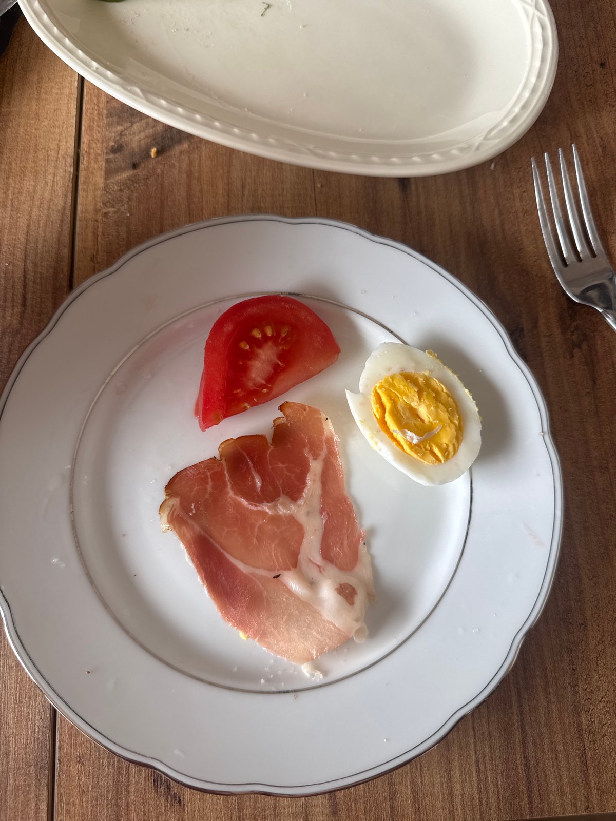 Morning meal documented featuring egg, tomato, prosciutto on wooden table