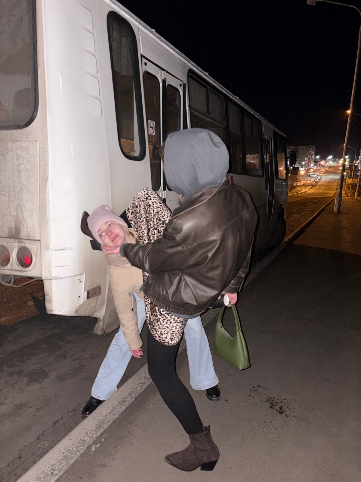 Two people interact near white vehicle in Ust-Ilimsk nighttime