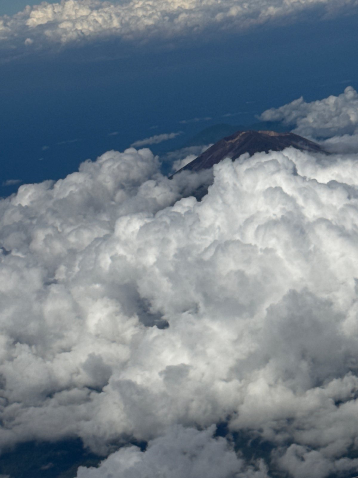 Aircraft passenger witnesses clouded mountain peaks over Bangli, Indonesia