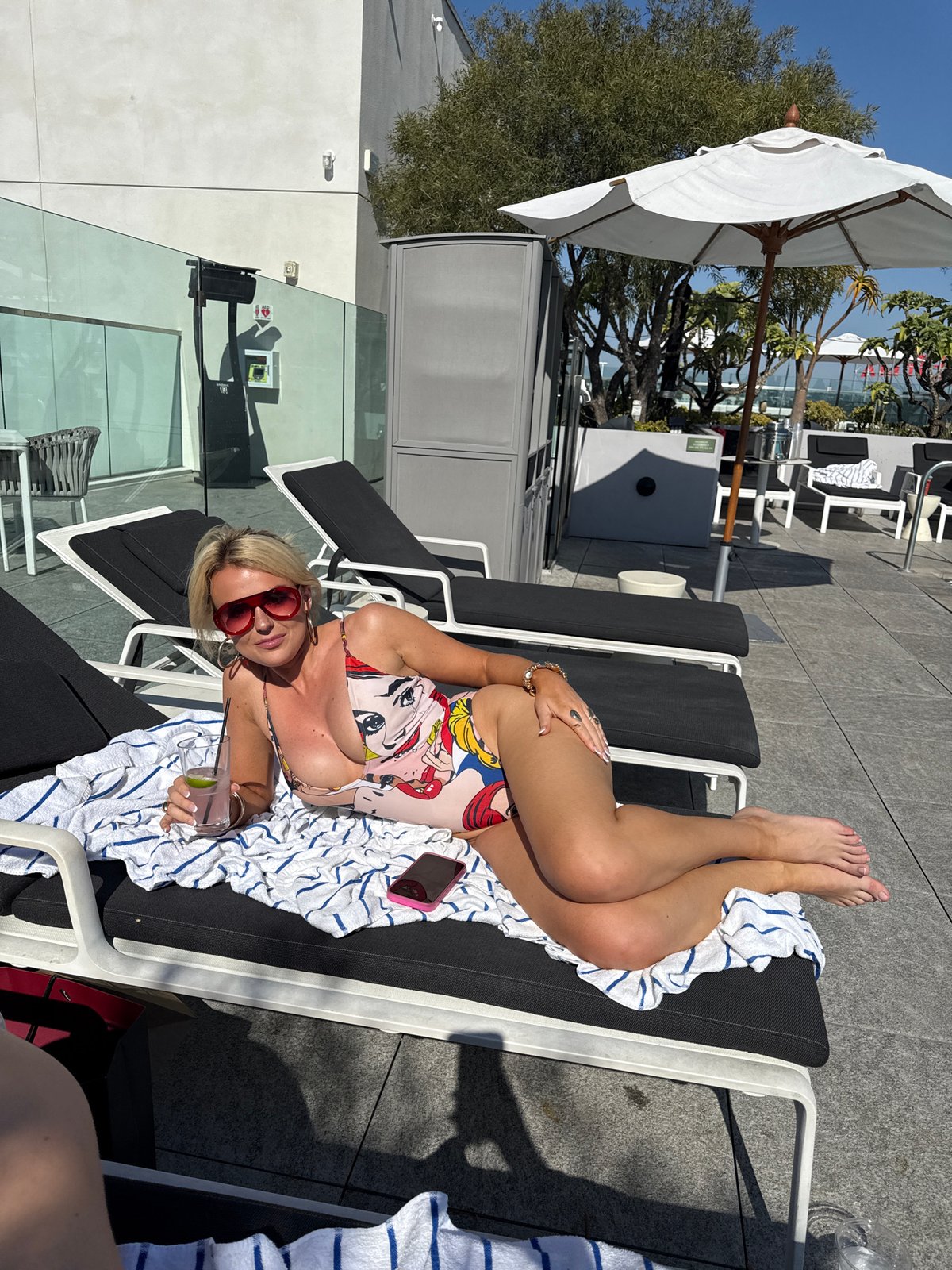 Woman relaxes poolside in comic swimsuit and heart sunglasses
