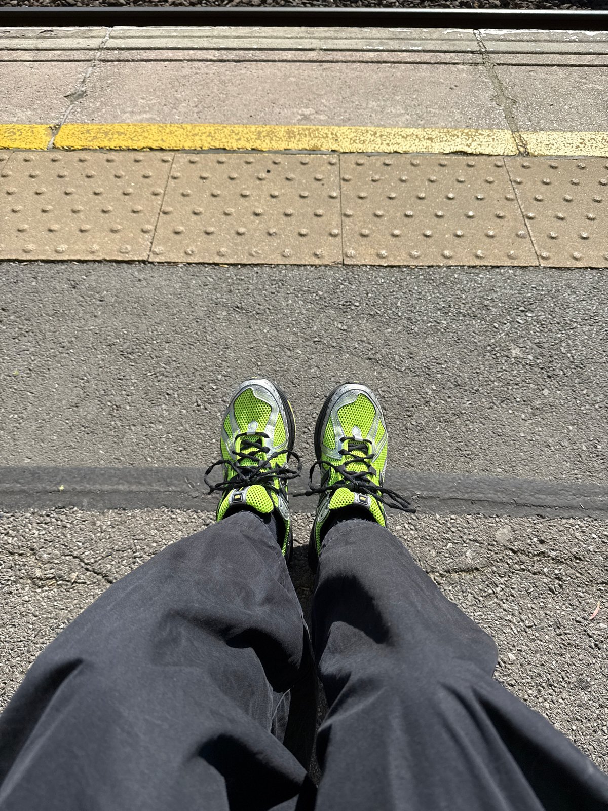 Commuter in green sneakers waits on London train platform