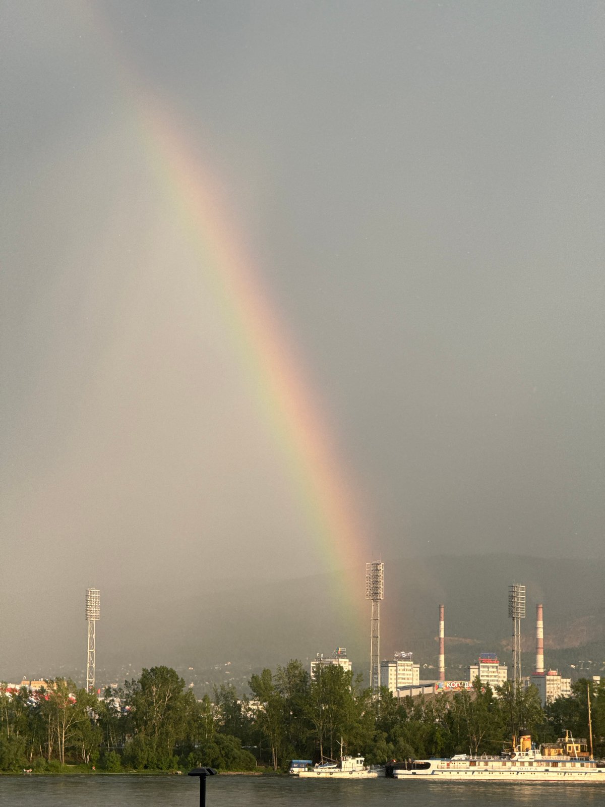 Rainbow arcs over Yenisei River during busy Krasnoyarsk waterfront afternoon