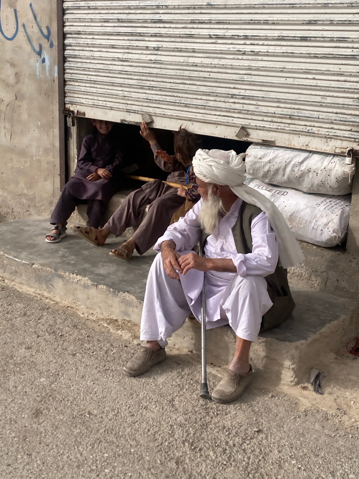 Elderly man in traditional dress sits with walking stick in Quetta