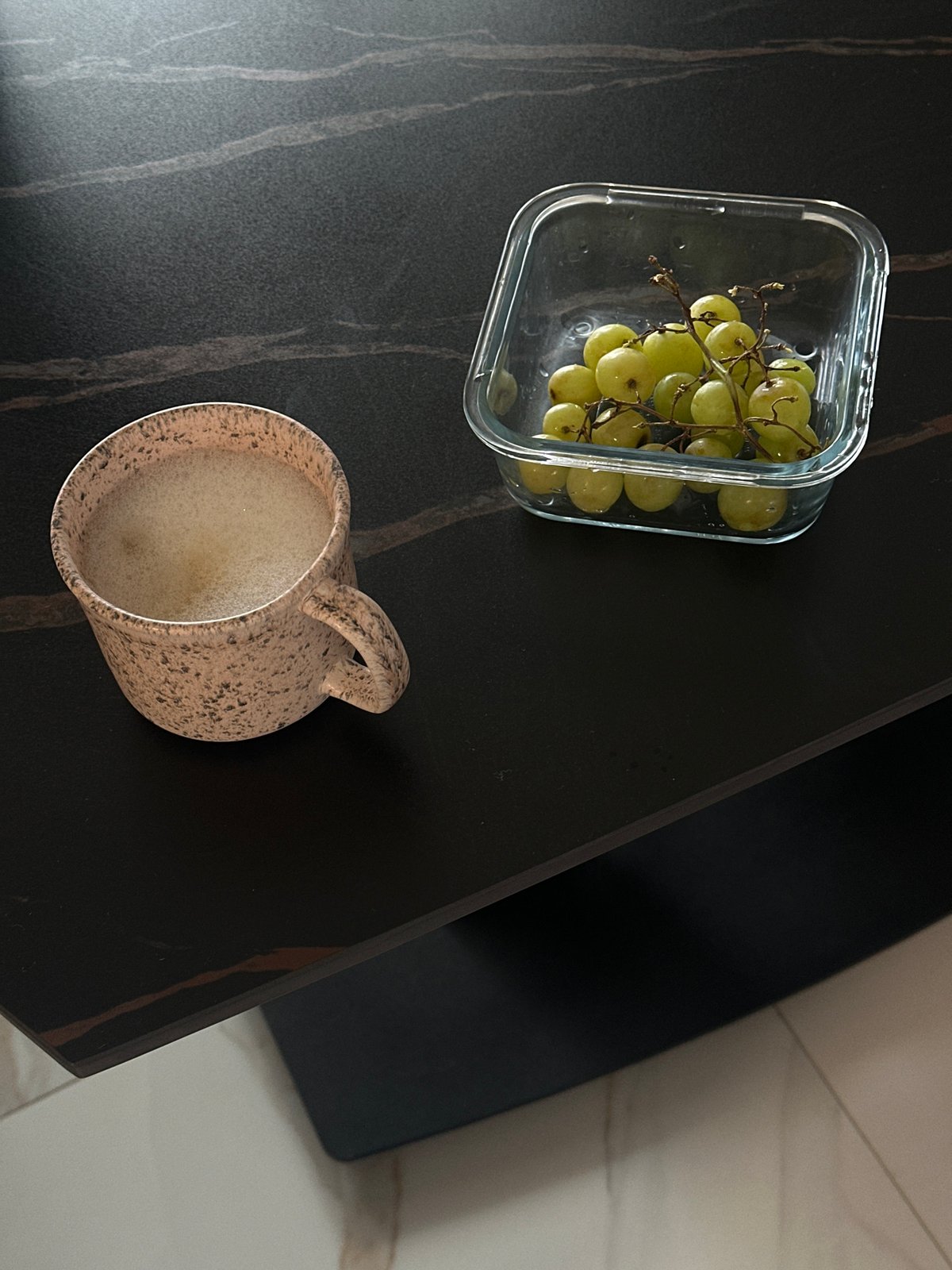 Green grapes and mug spotted on marble table in Sofia
