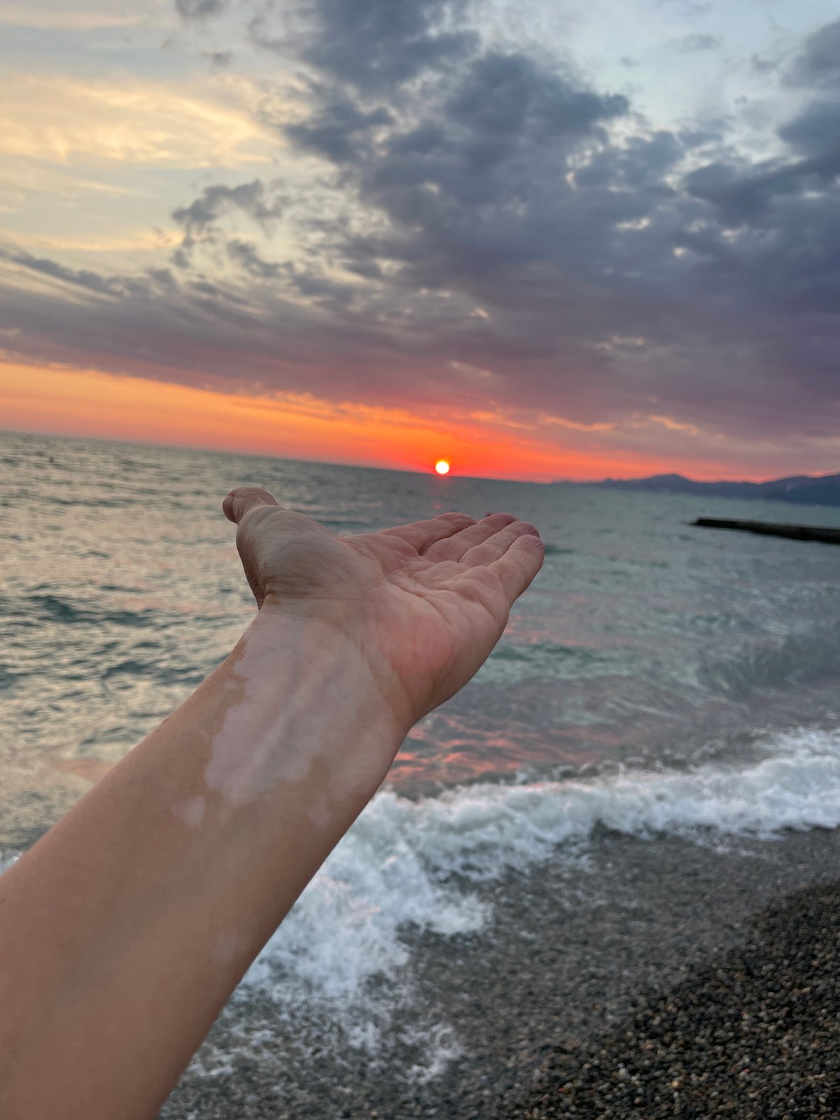 Woman captures sunset selfies on pebbled ocean beach