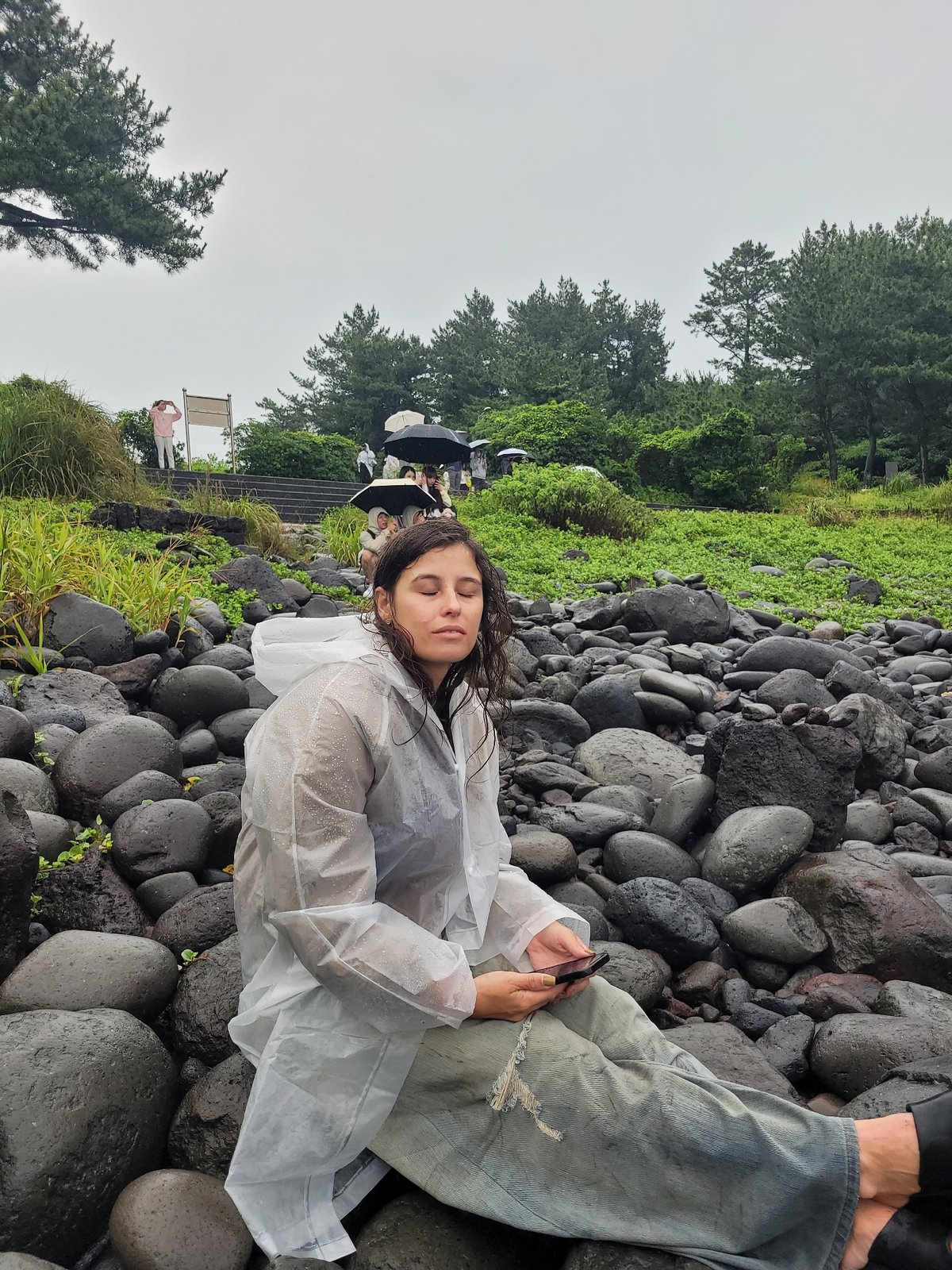 Rainy morning on Jeju's volcanic coast, umbrellas out