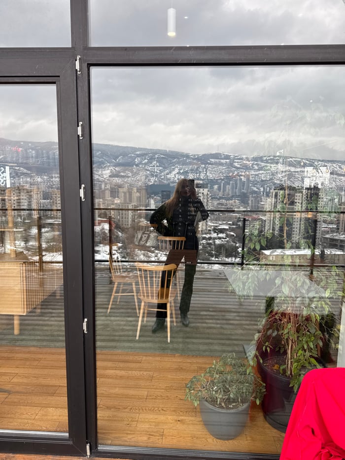 Woman photographs herself on Tbilisi balcony overlooking cityscape