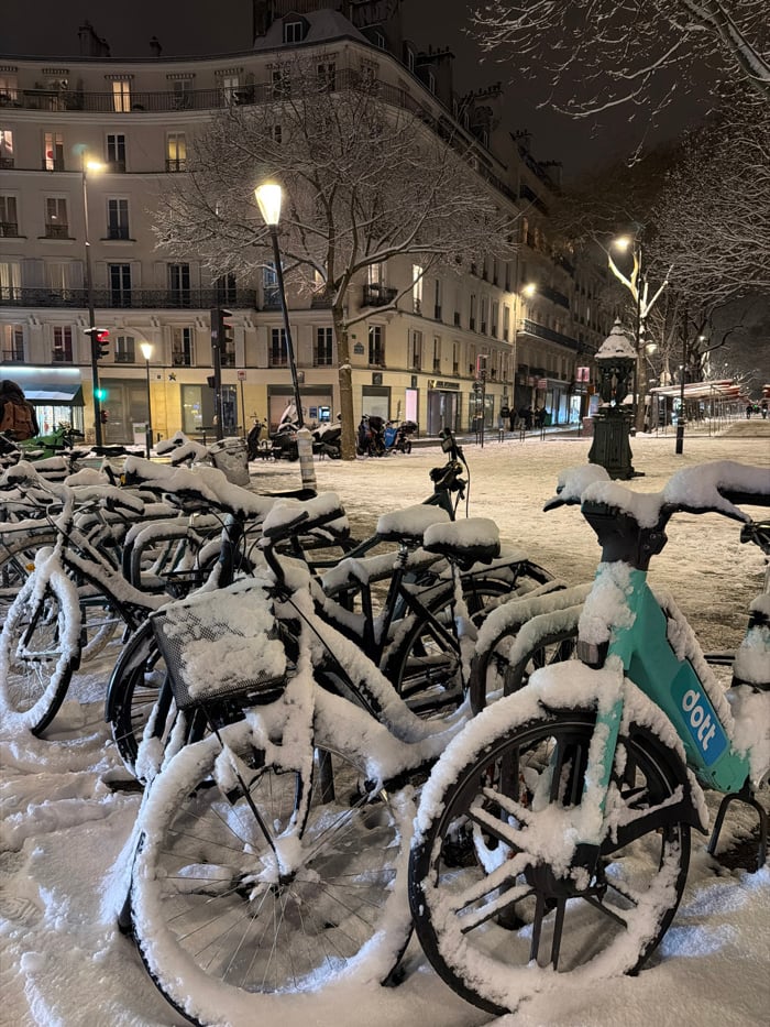 Snow blankets Paris streets, bicycles during January evening