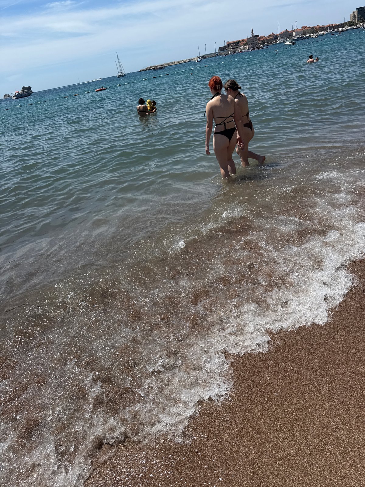 Budva beach in full summer swing — boats, parasails, and crowds