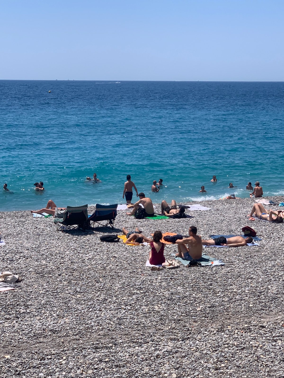 Packed summer day on Nice's pebble beach, Mediterranean in full swing