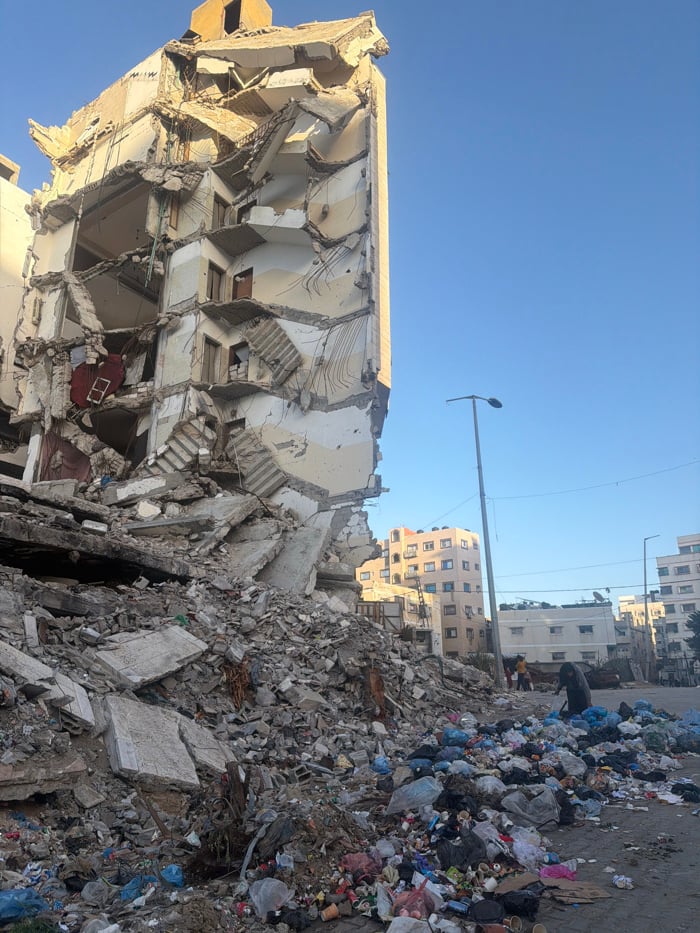 Damaged buildings observed in Gaza with pedestrians, debris visible