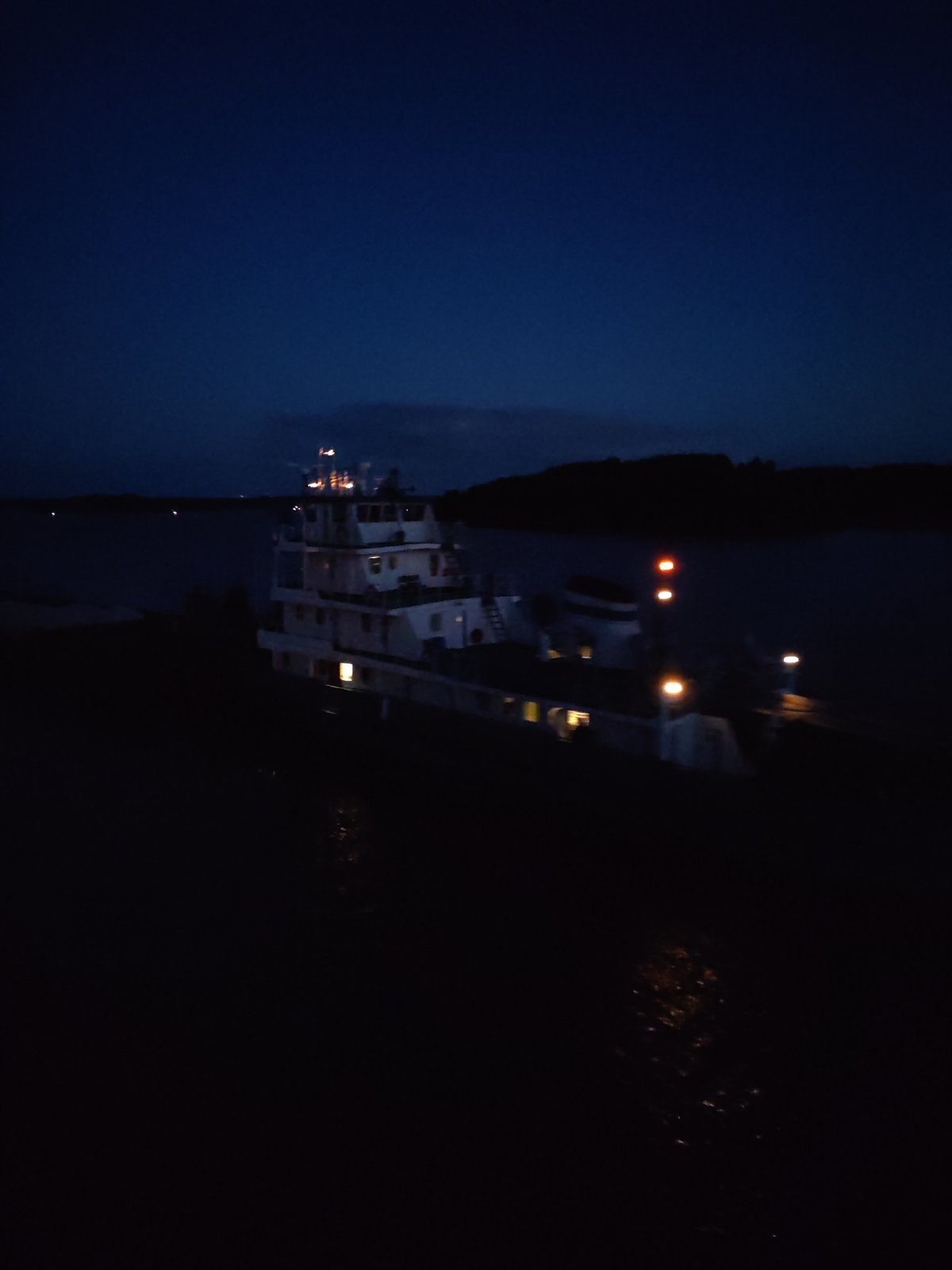 Tugboat pushes barge upriver at night near Нова, Russia