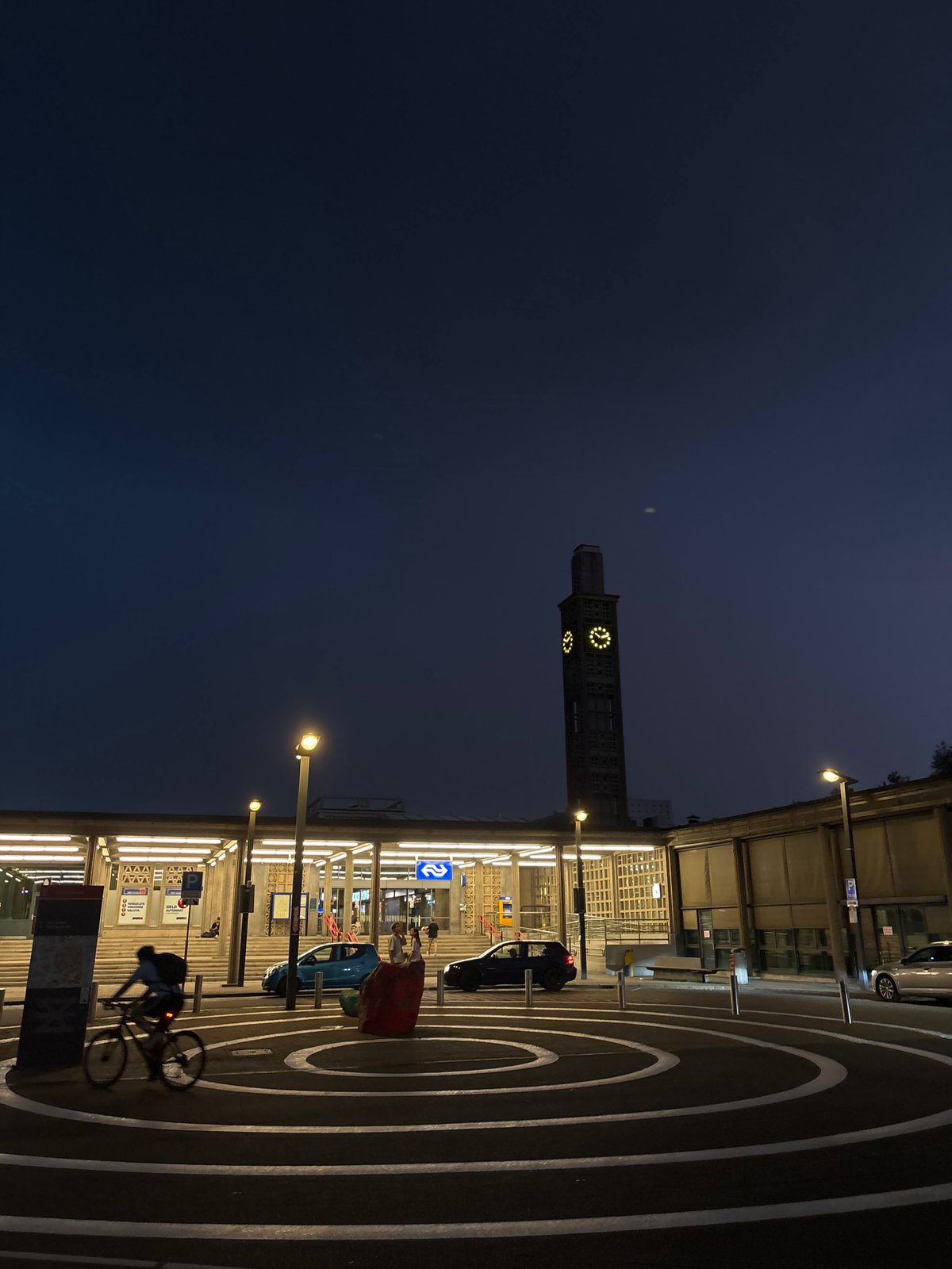 Cyclist passes Enschede Central Station at dusk