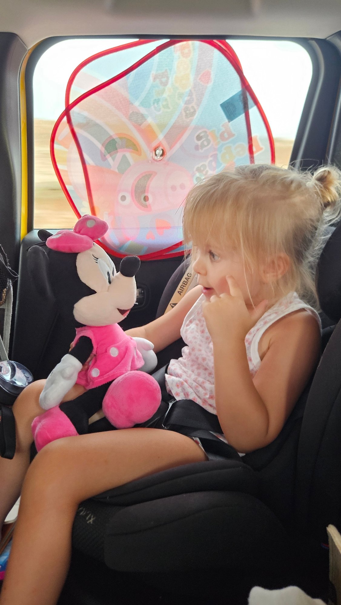 Minnie Mouse plush in hand, pointing from a car seat in Spain