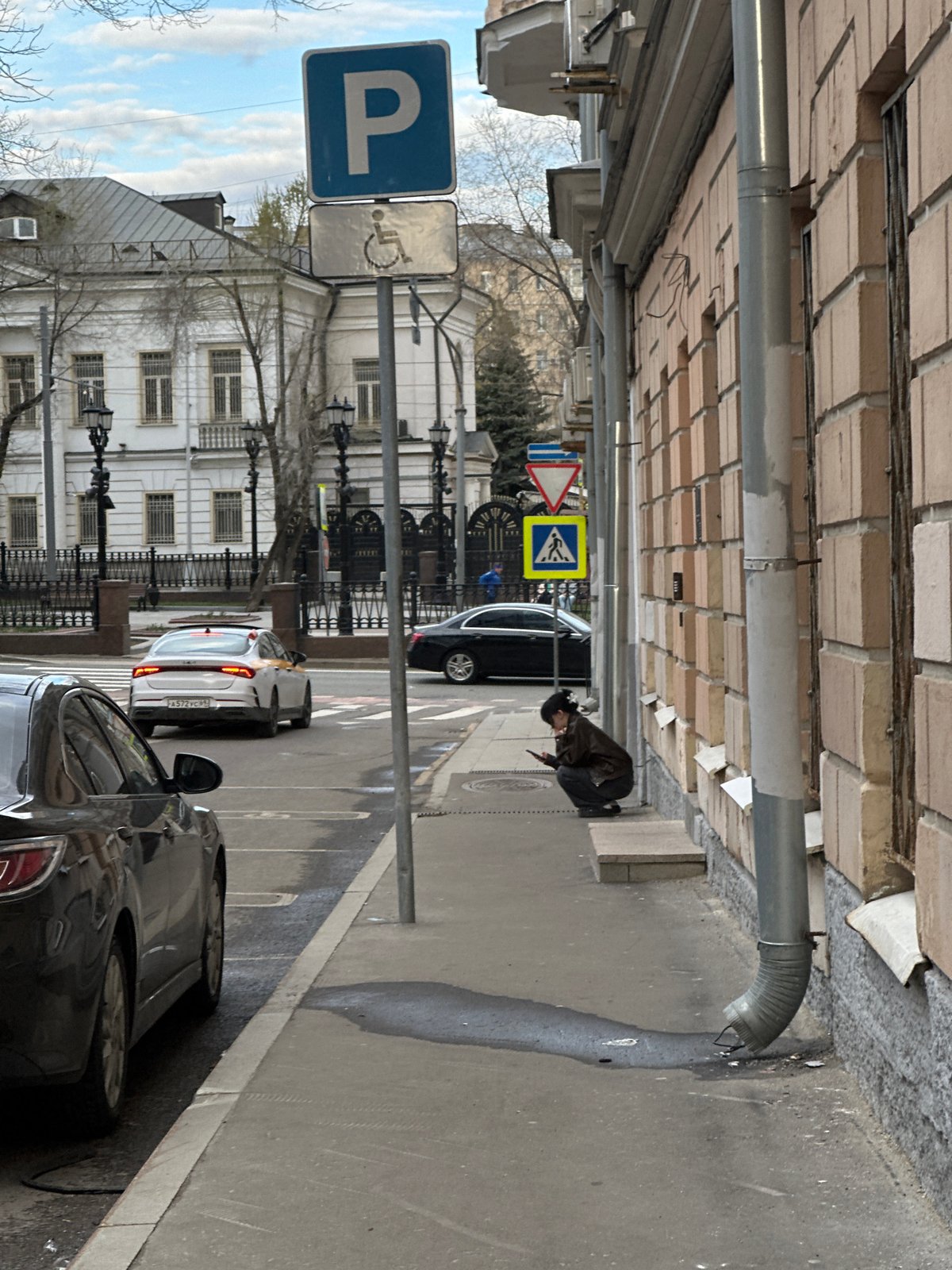 Woman crouches near car on Moscow sidewalk