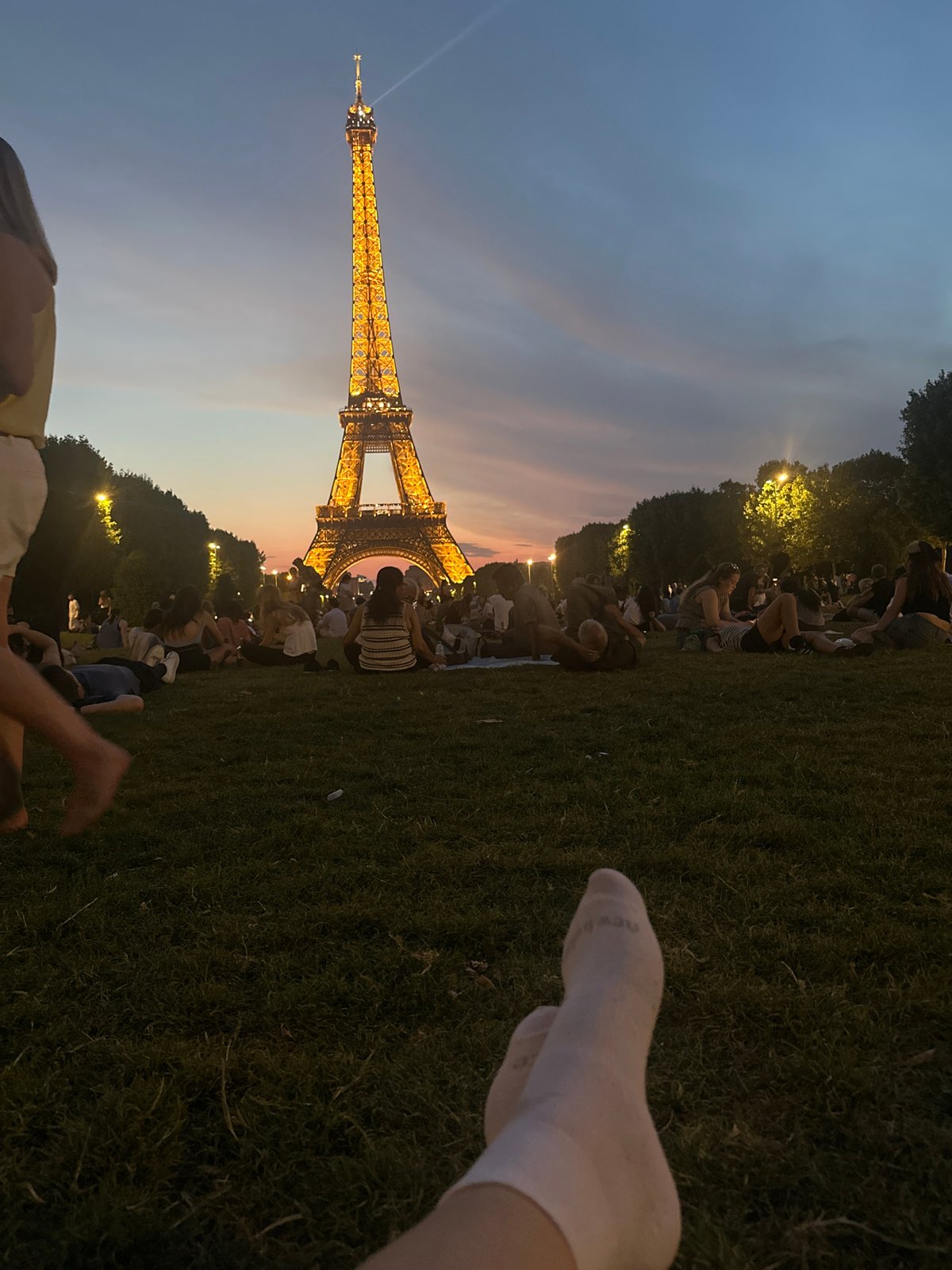 Eiffel Tower glows at dusk over a relaxed Champ de Mars crowd.
