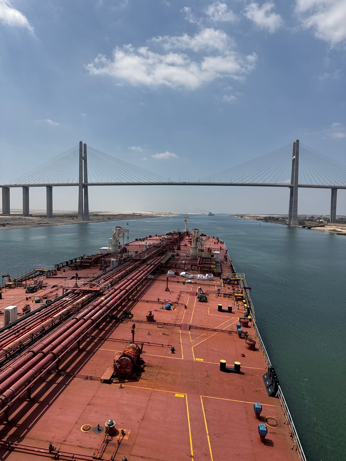 Red cargo ship transits the Suez Canal beneath a cable-stayed bridge