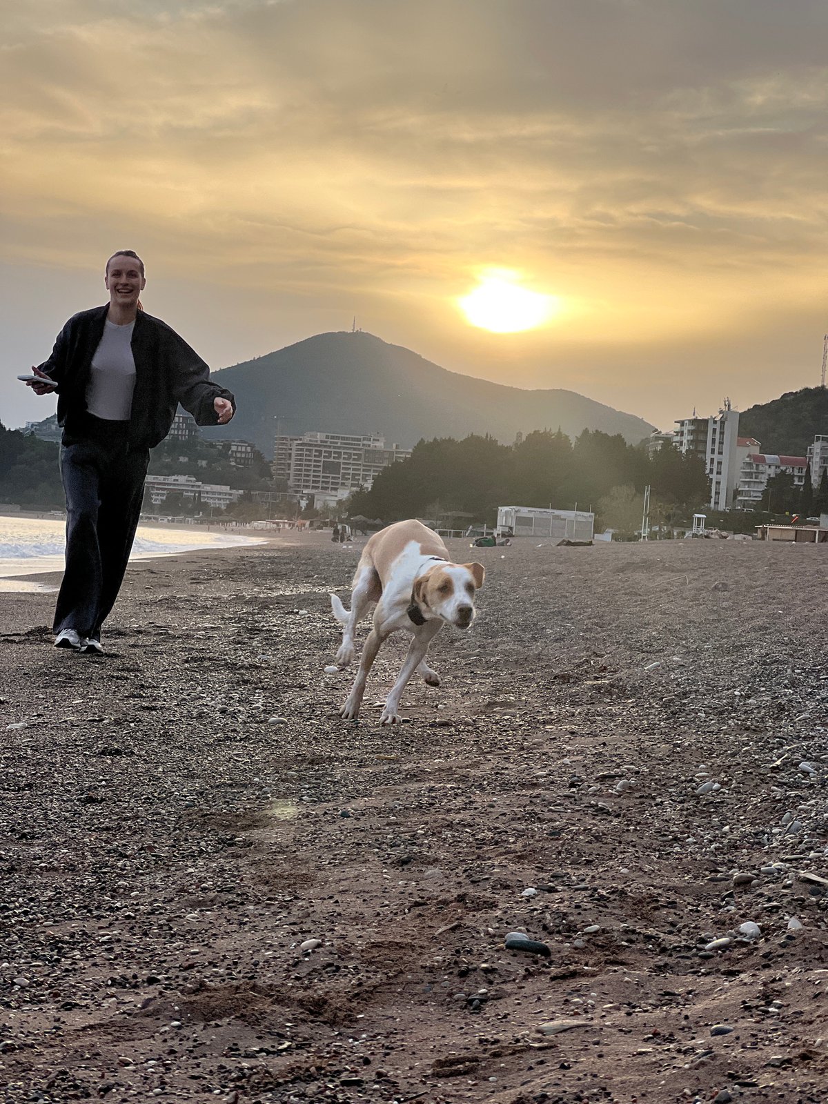 Person photographs dog on Montenegro beach at sunset