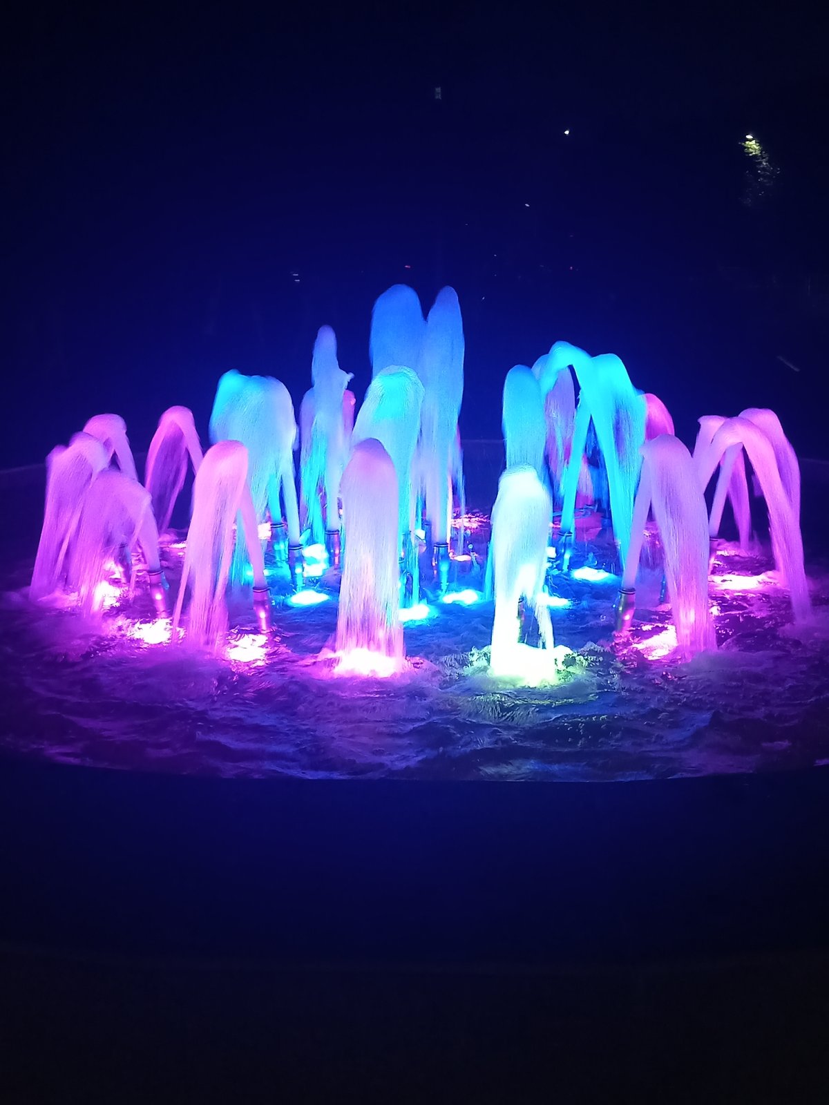 Lit fountain and park walkway in Rudny at night
