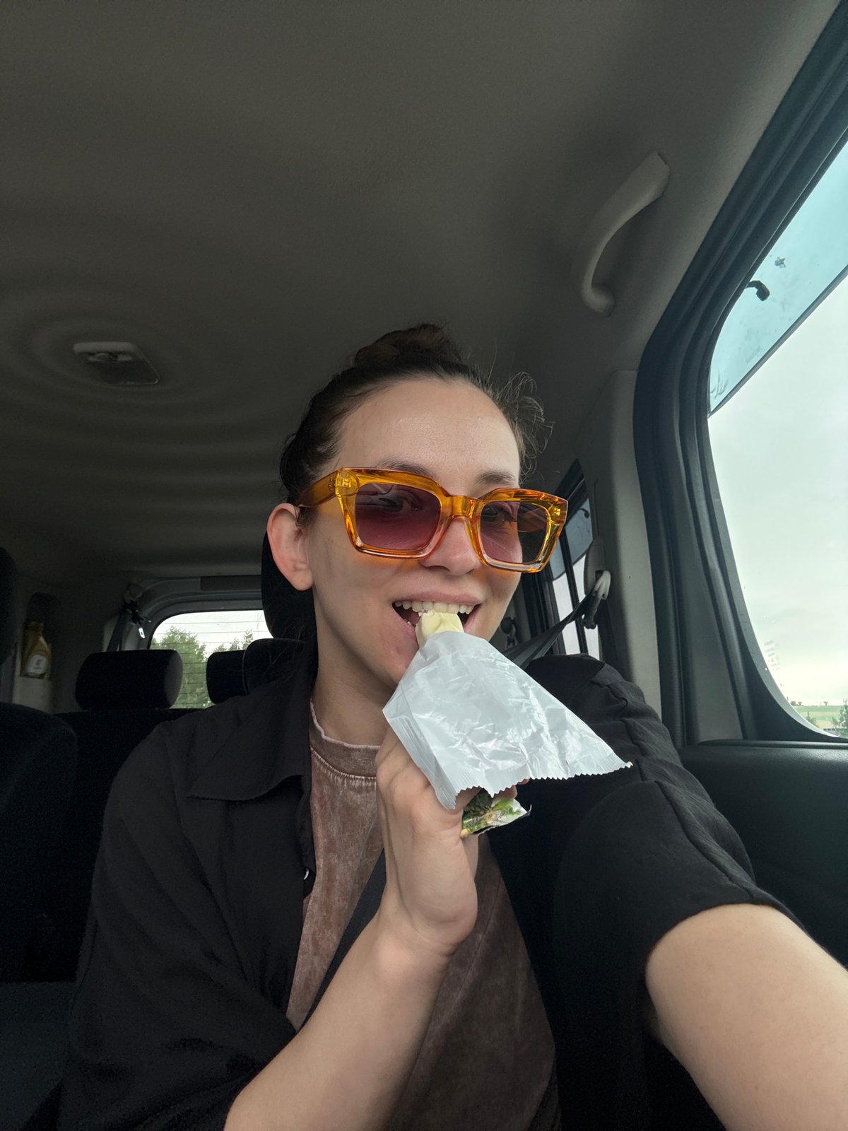 Person in orange sunglasses eats from bag in car