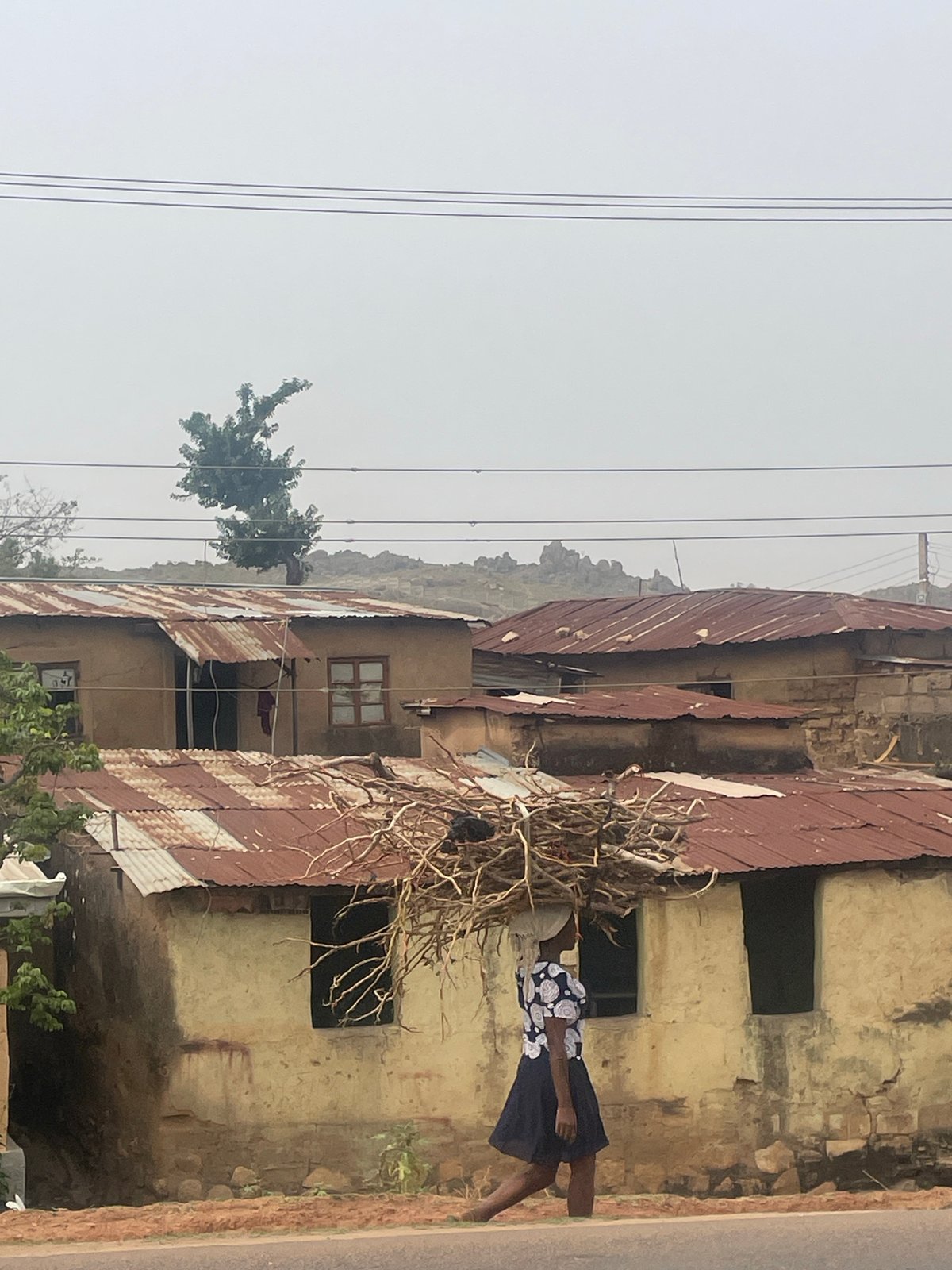 Woman carries branches near weathered building in Jos, Nigeria