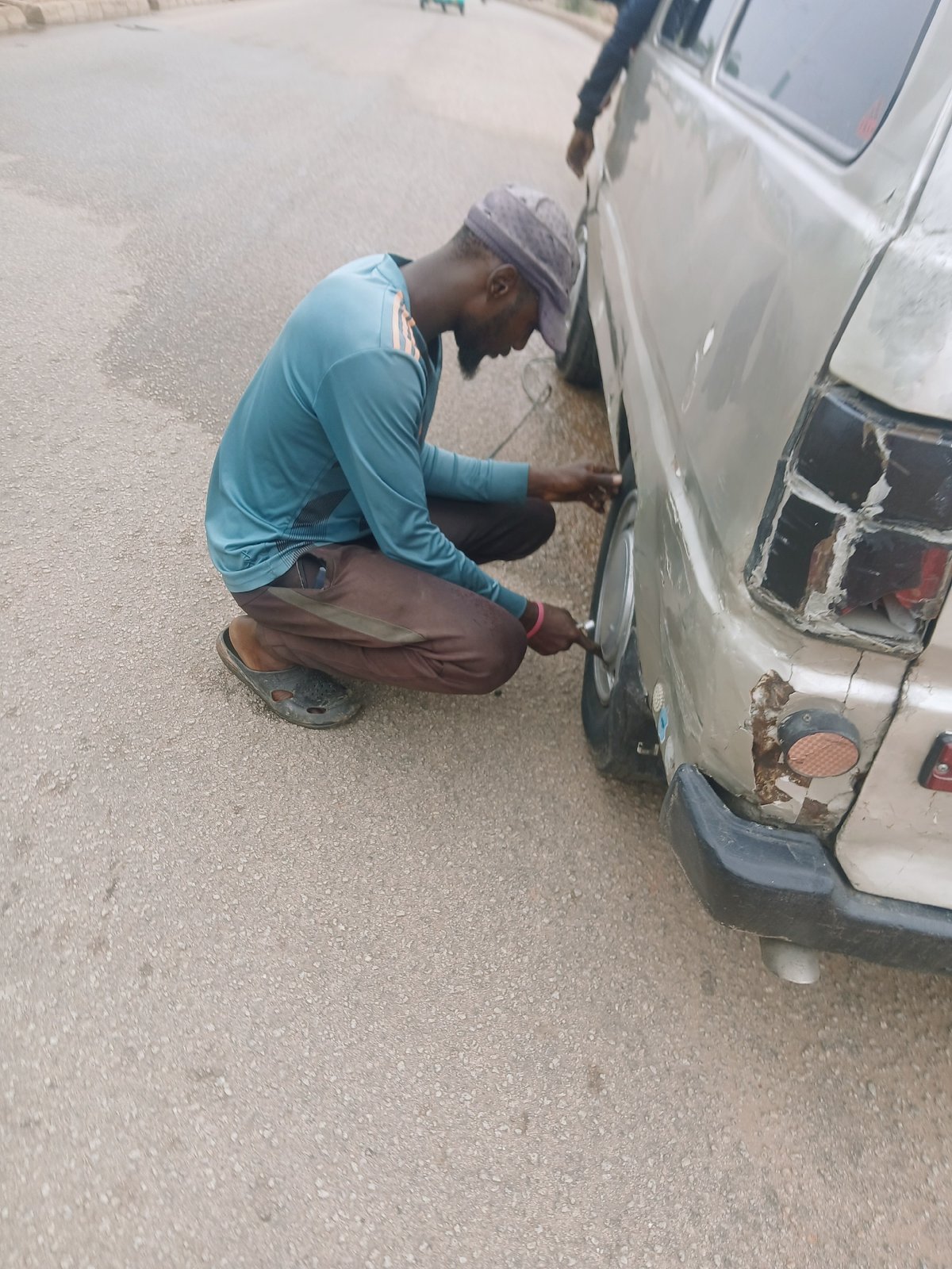Man performs vehicle maintenance on gray car in Bukuru