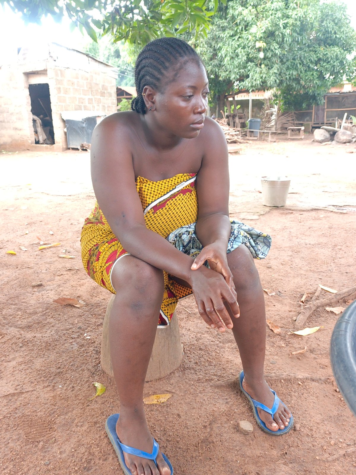 Woman in traditional dress sits outdoors on wooden stool
