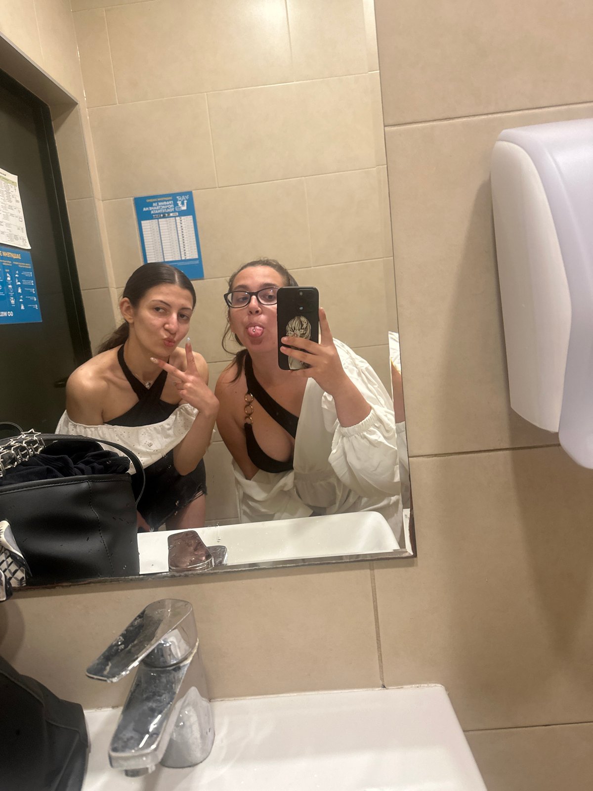 Two women take mirror selfies in Pomorie restroom
