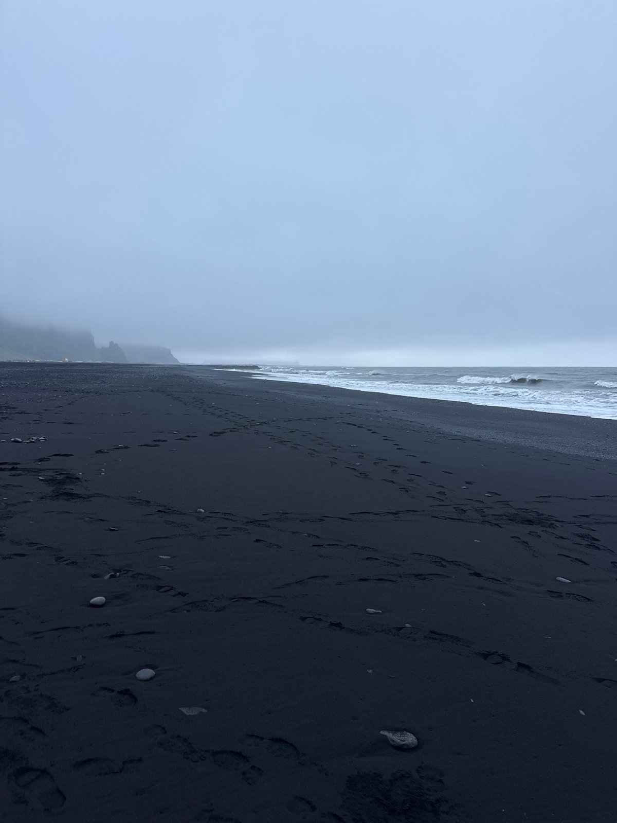 Visitor documents dramatic Reynisfjara black beach during overcast evening