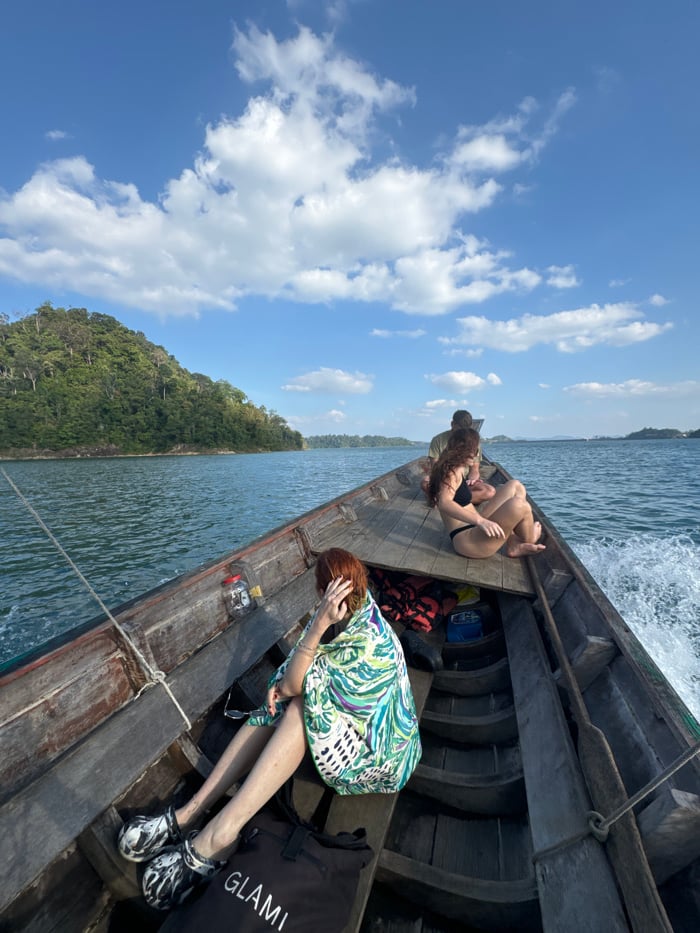 Longtail boat crosses large lake under partly cloudy skies