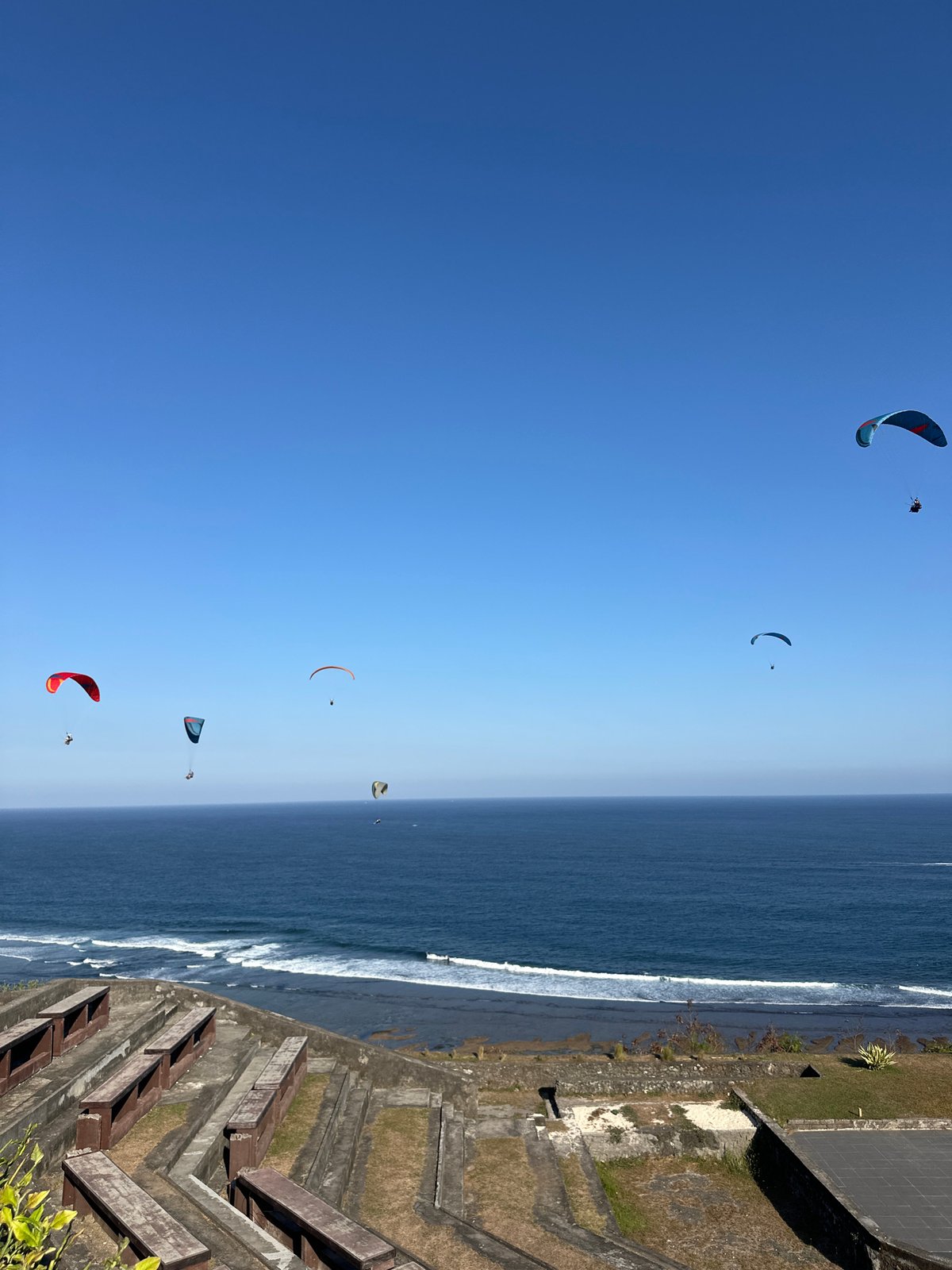 Uluwatu's clifftop amphitheater, cave structure, and paragliders on a clear morning