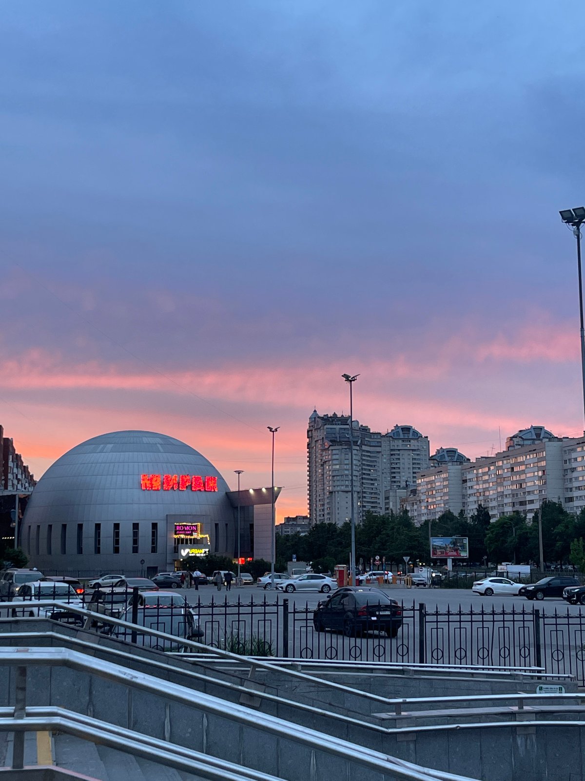 Dusk in a Soviet-era city district, neon Cyrillic signs lit up