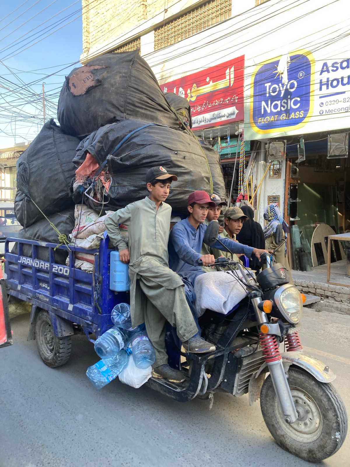 Three men ride overloaded motorcycle with trailer in Quetta