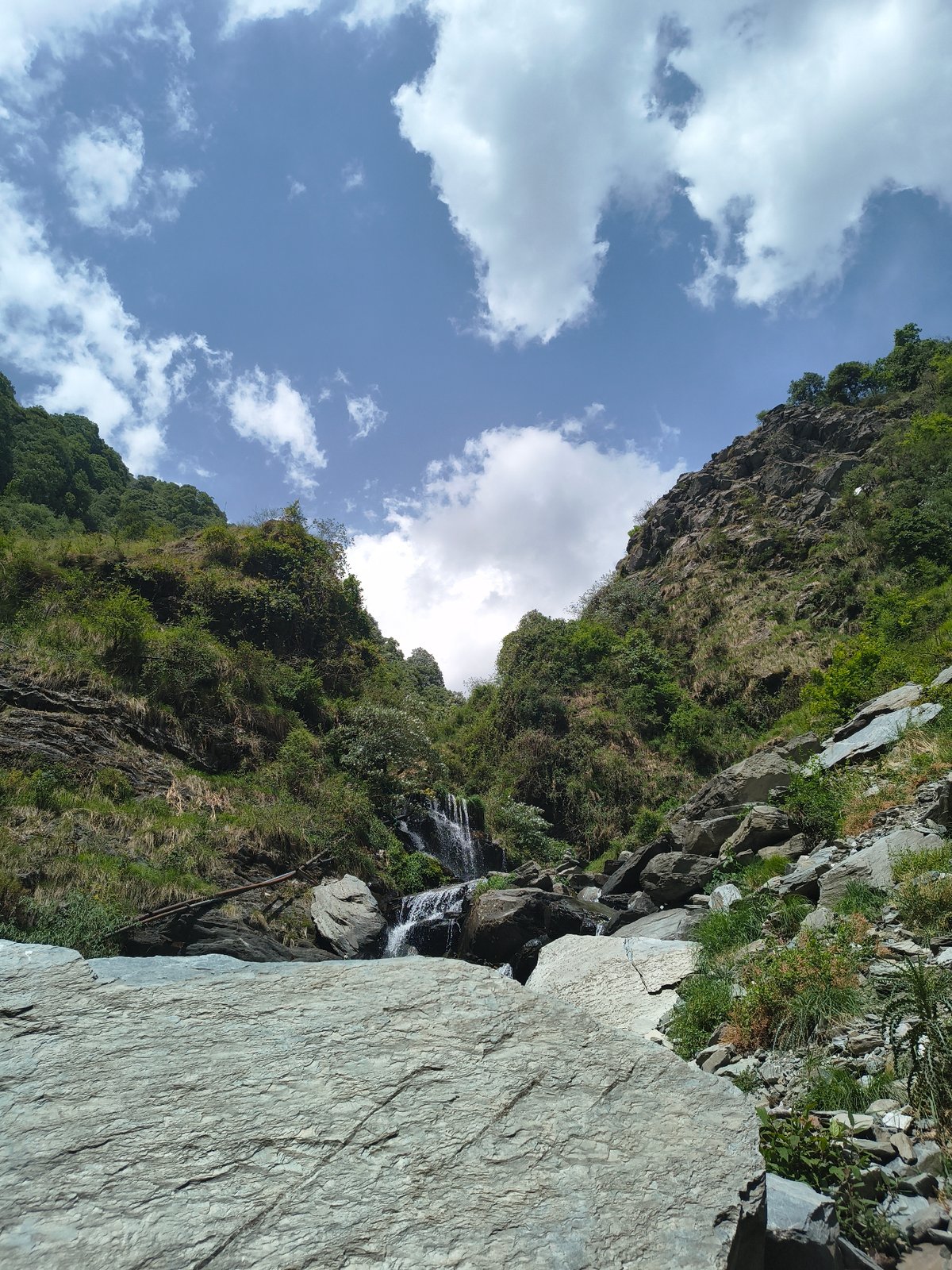 Small waterfall flows down rocky cliff in Bhagsu, India