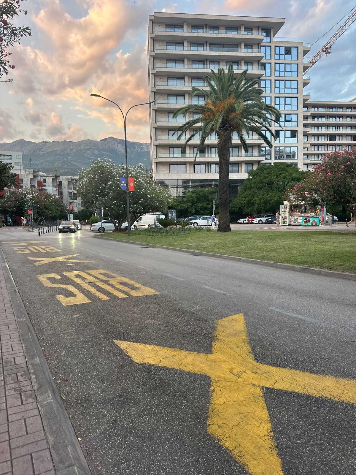 Budva street at dusk — scooters, bus stops, and mountain views
