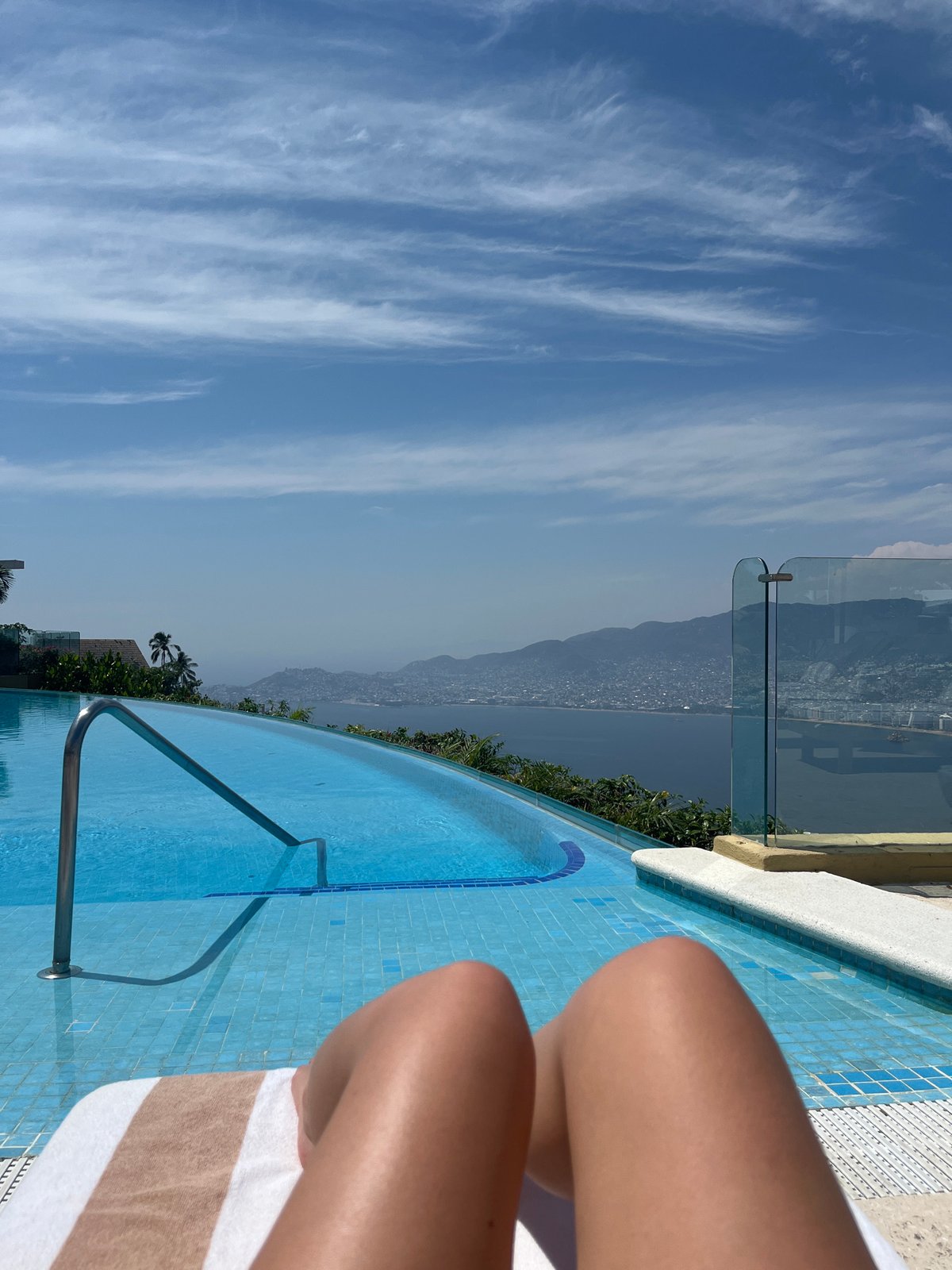 Person relaxes at infinity pool overlooking Acapulco coastline