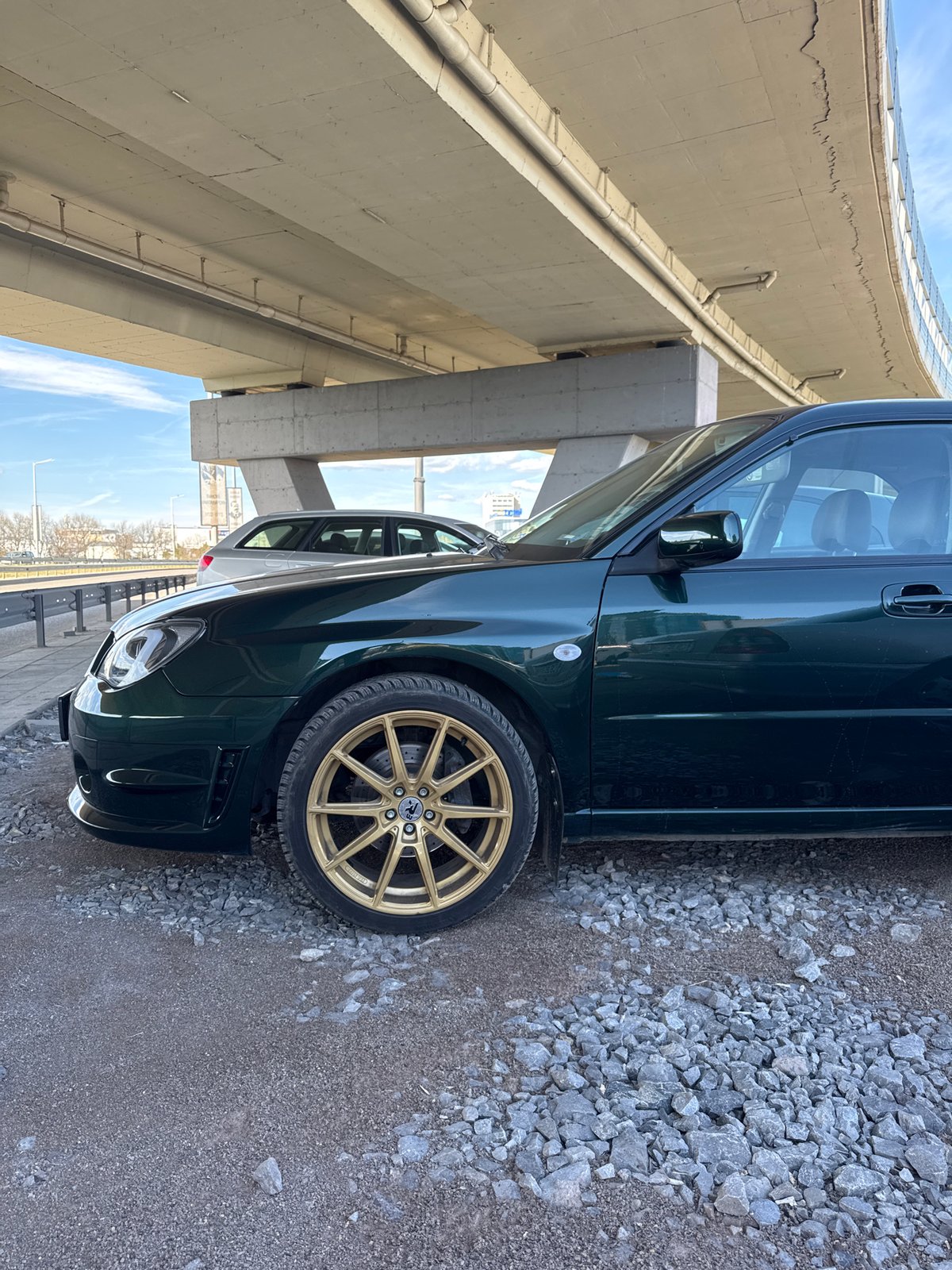Green car with gold rims parked under Sofia bridge