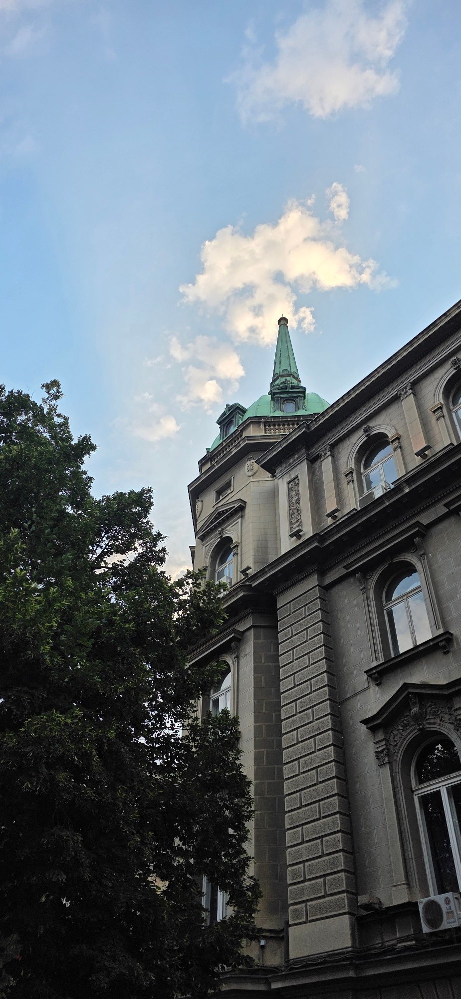 Historic stone building facade alongside a lush tree in Belgrade