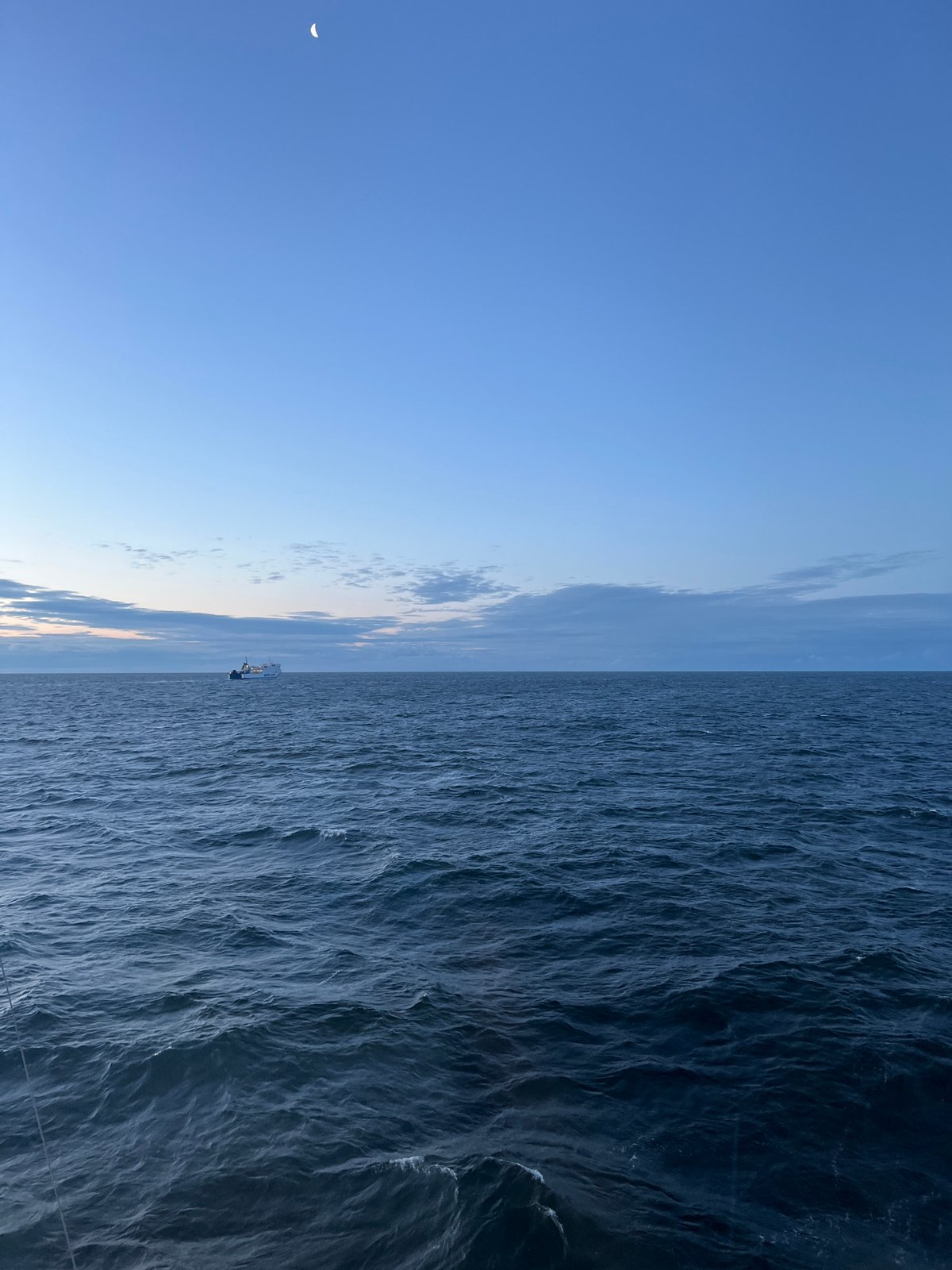 Crescent moon rises over a still ocean at dusk